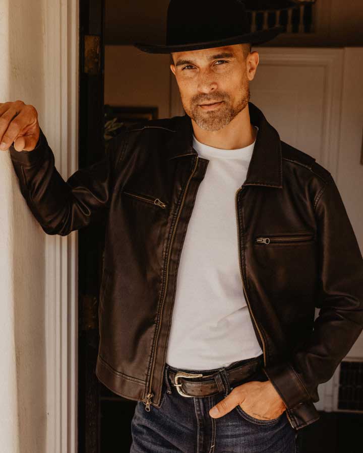 man standing with leather jacket and hat.